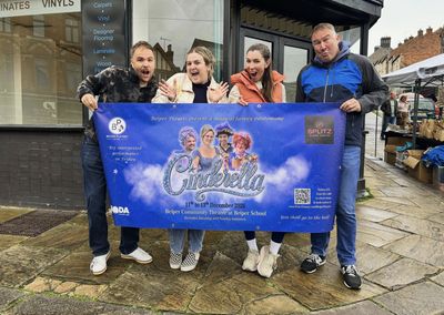 Four of the cast pulling faces on a Belper street as they hold up the Cinderella banner, which gives the dates and says tickets are £15.